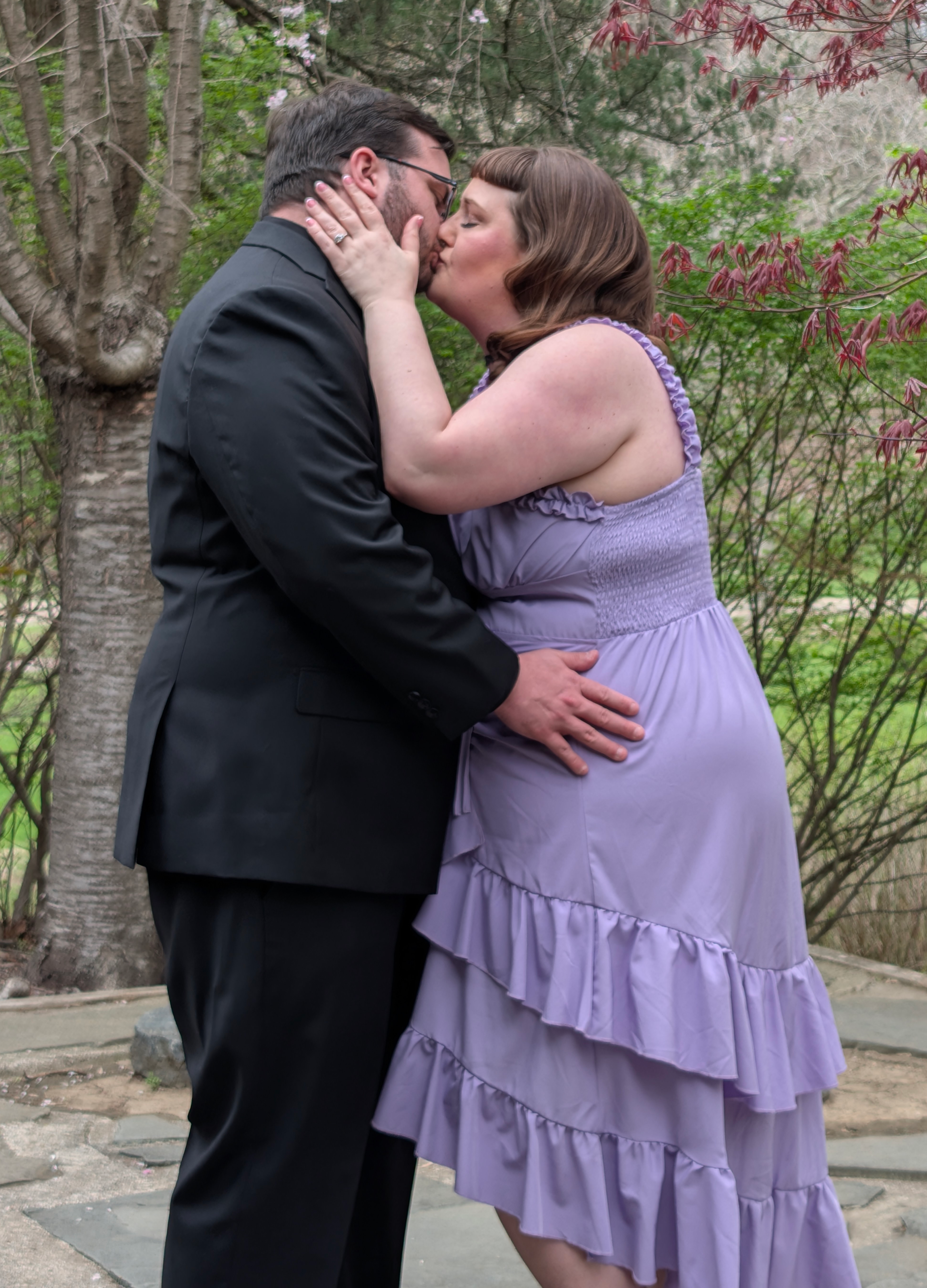 Marina and Randall kissing near trees in bloom.
